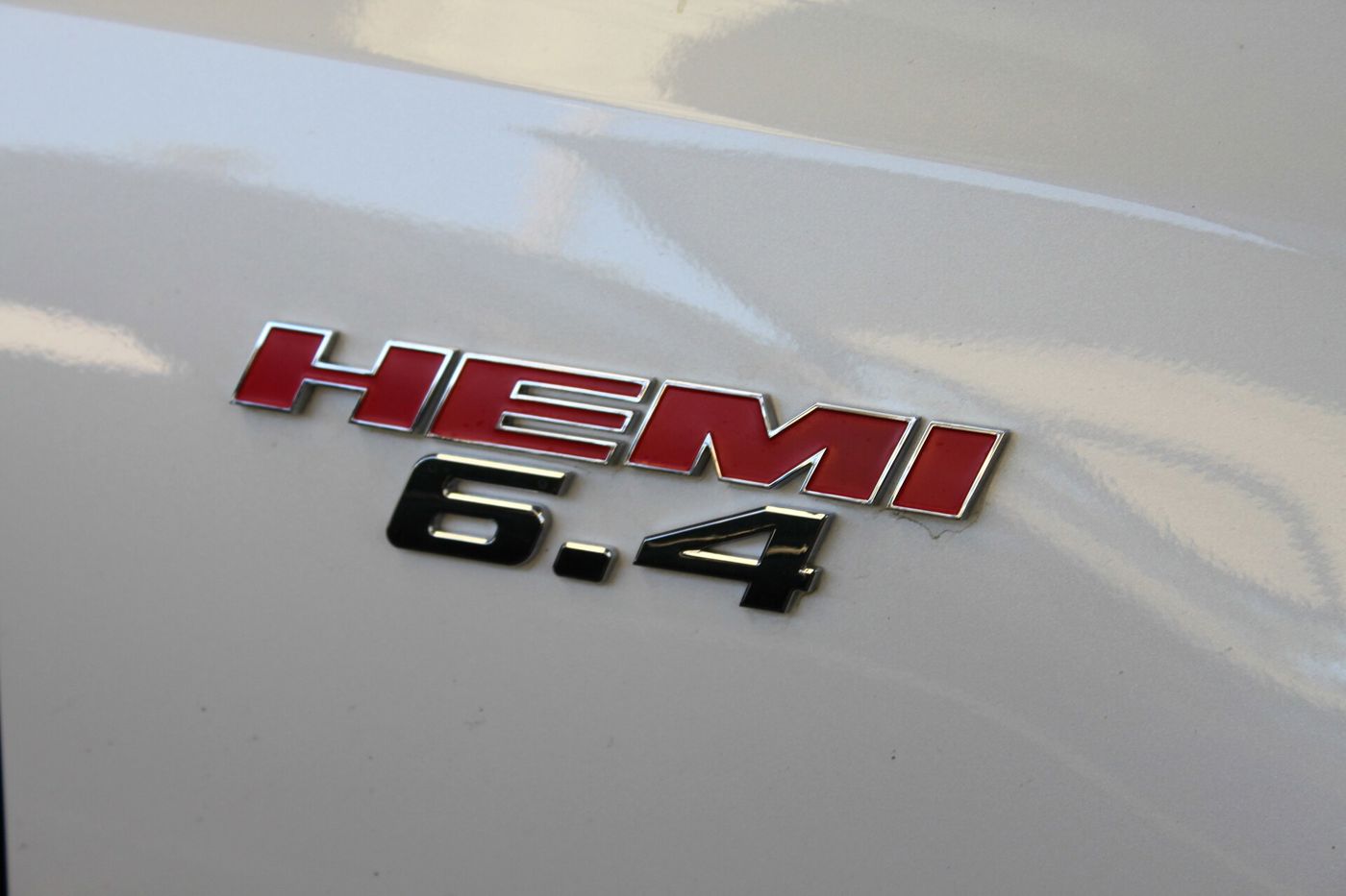 Close-up of a red and chrome HEMI badge above a black 6.4 on the white front fender of a Chrysler 300 SRT8