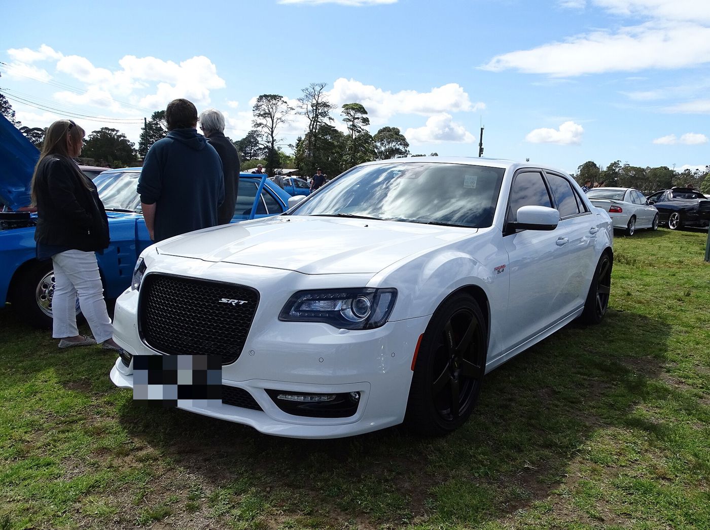 White facelifted Chrysler 300 SRT with the larger black mesh grille and SRT badge, on grass at a car show