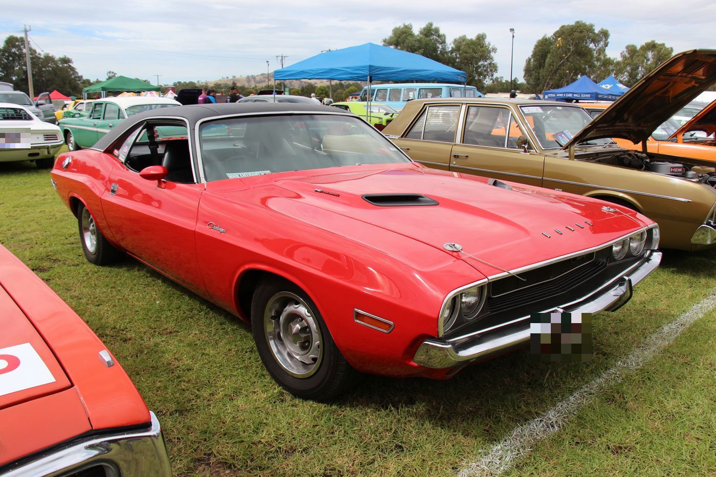 Red 1970 Dodge Challenger hardtop with black vinyl roof and twin hood scoops, front three-quarter at an outdoor show