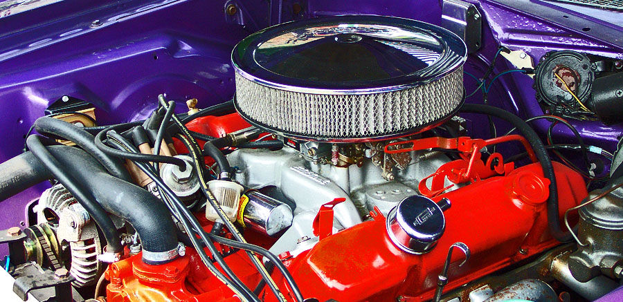 Close view of a 1970 Dodge Challenger V8 with orange-red valve covers and chrome open-element air cleaner in a purple engine bay