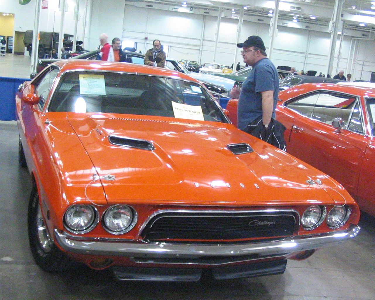 Orange 1973 Dodge Challenger with twin hood scoops at an indoor classic-car auction