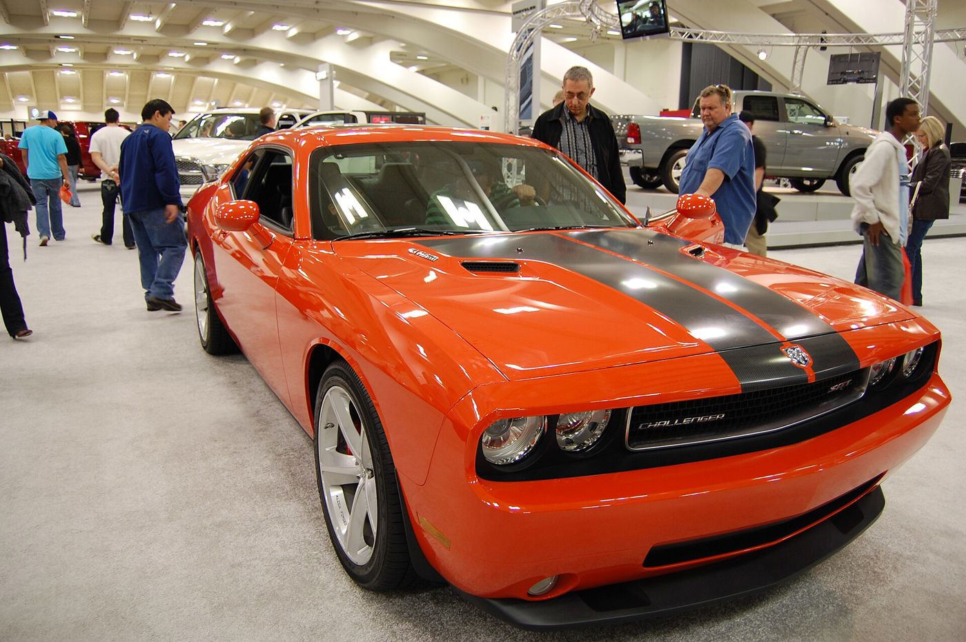 Orange 2009 Dodge Challenger SRT8 with black hood stripes and hood scoop, at an auto show