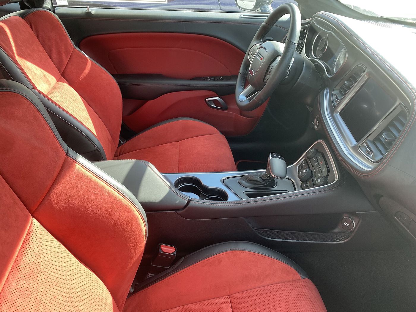 Front seats and centre console of a 2021 Dodge Challenger with red suede-and-leather seats and the driver-angled dashboard