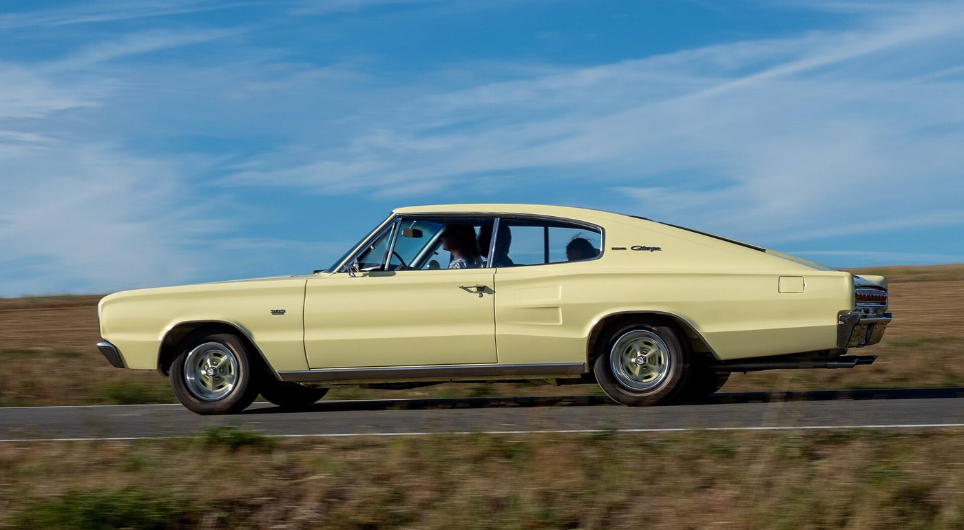 Pale yellow 1967 Dodge Charger driving past, showing the long fastback roofline in profile