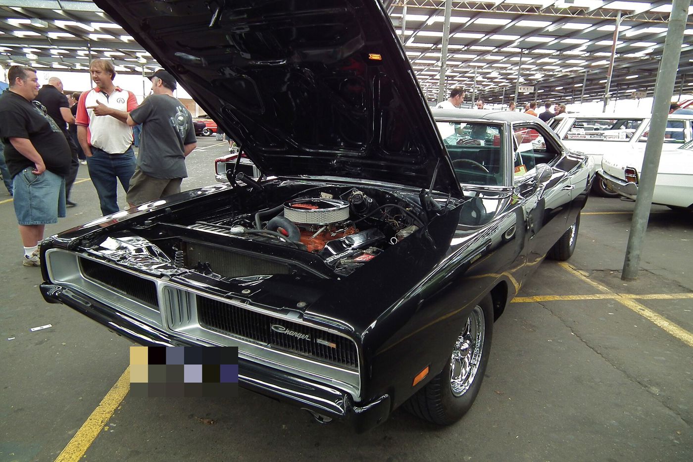 Black 1969 Dodge Charger at a car show with its hood raised to show the orange V8