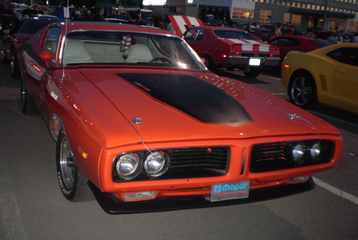 Orange 1971 Dodge Charger with blacked-out hood and quad headlamps, seen from the front at night