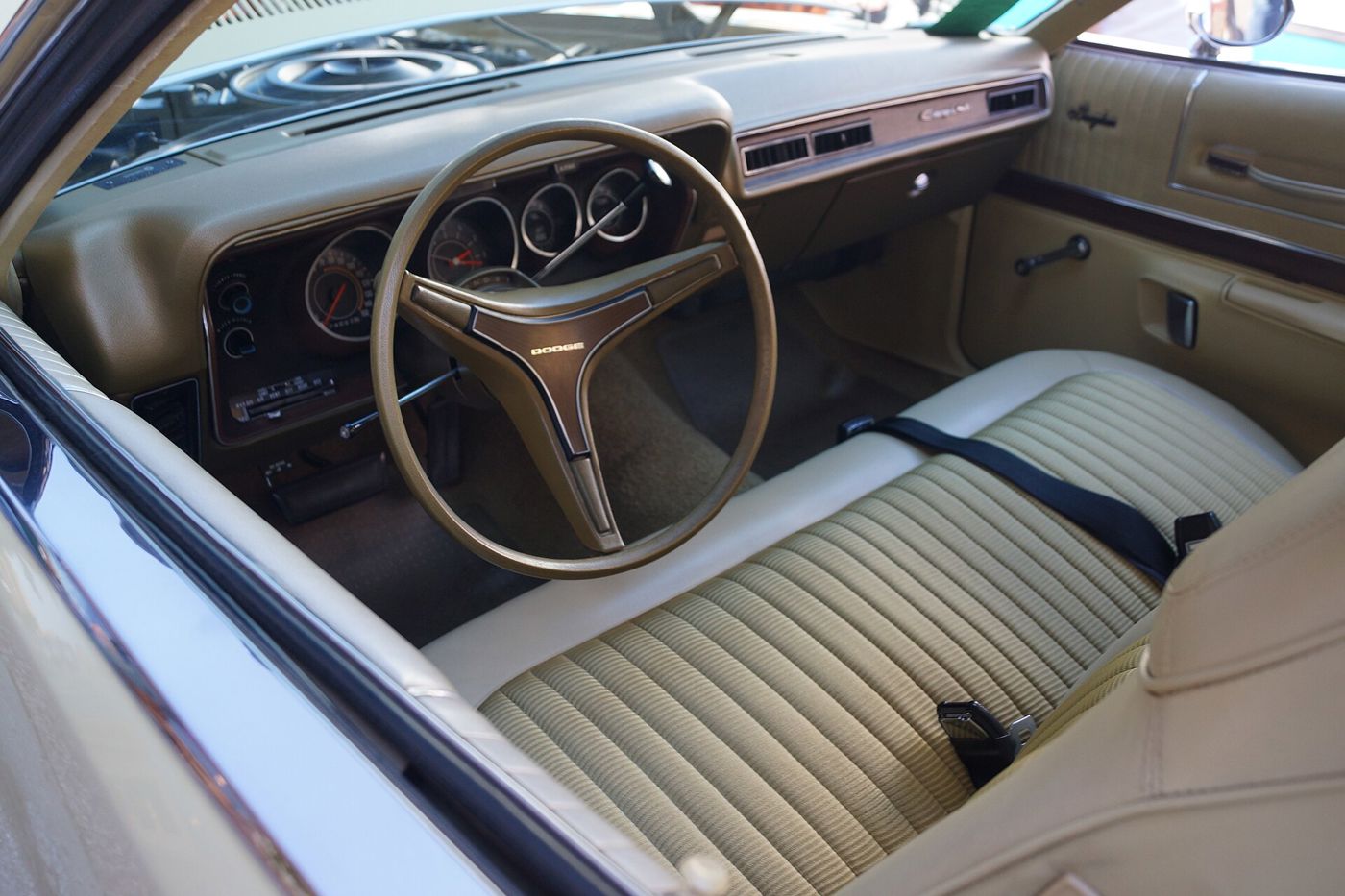 Tan interior of a 1972 Dodge Charger SE seen through the door: bench seat, round gauges and three-spoke steering wheel