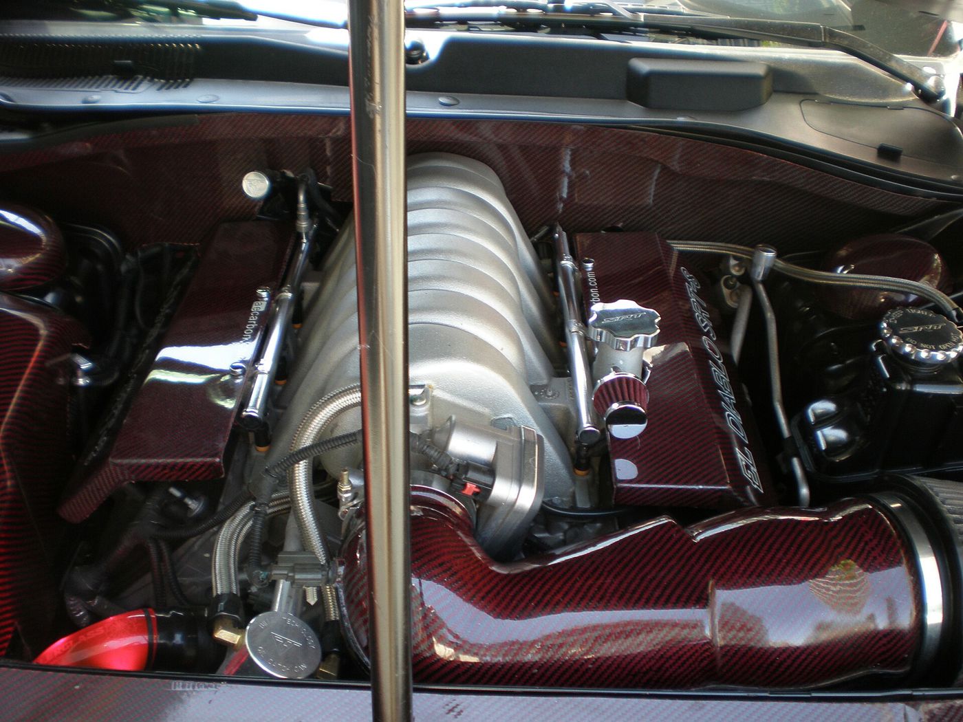 Engine bay of a modified 2006 Dodge Charger SRT8 showing the silver Hemi intake manifold and red carbon-fibre intake tube