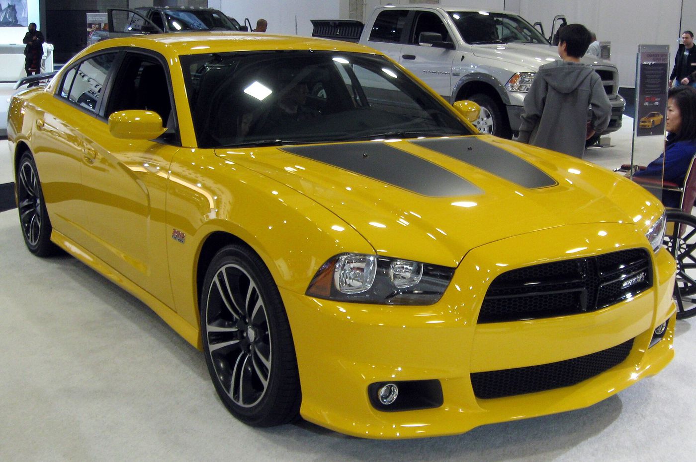 Yellow 2012 Dodge Charger SRT8 Super Bee with black hood stripe, displayed at an auto show