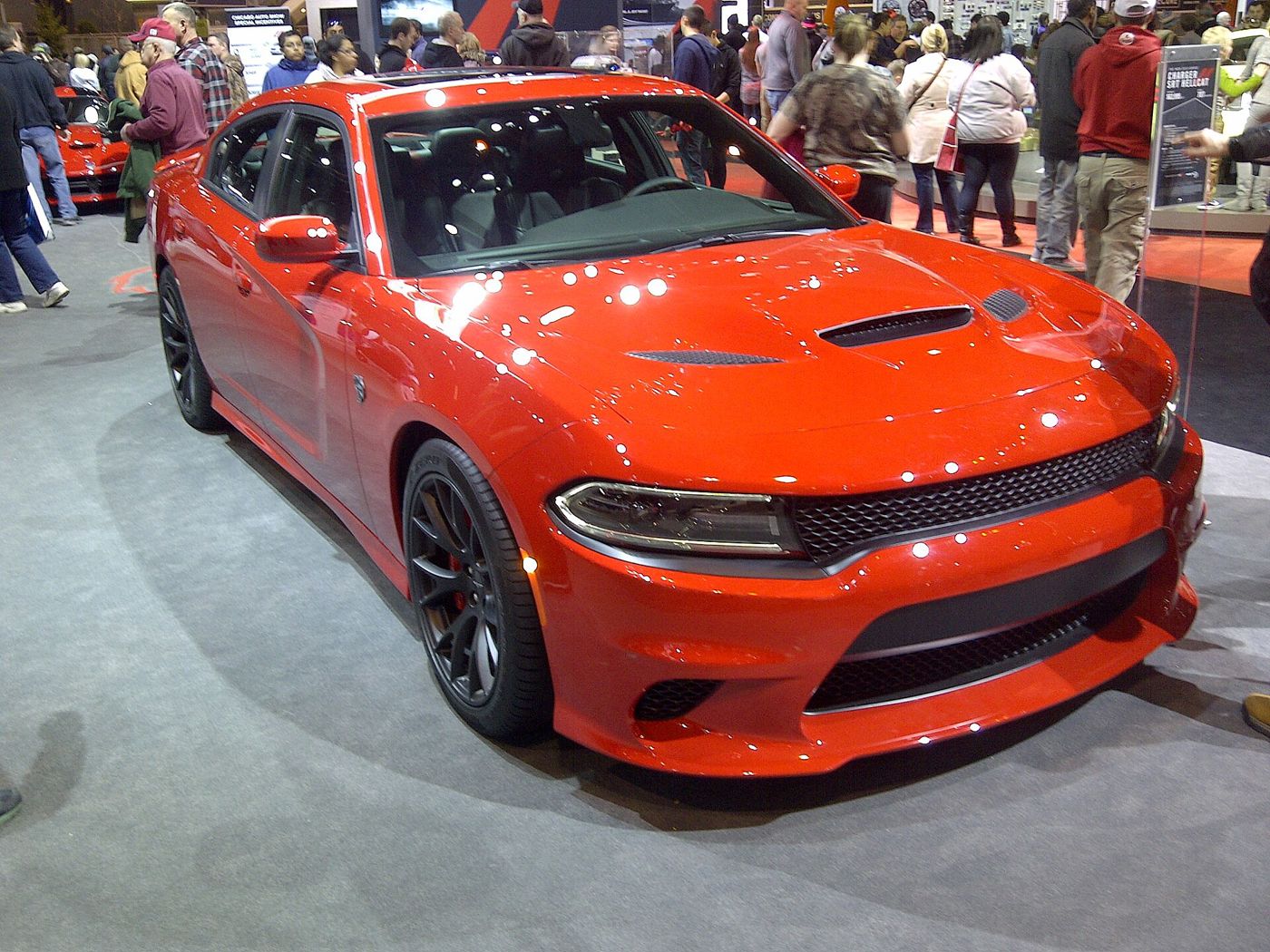 Orange-red 2015 Dodge Charger SRT Hellcat with vented hood, on an auto show stand