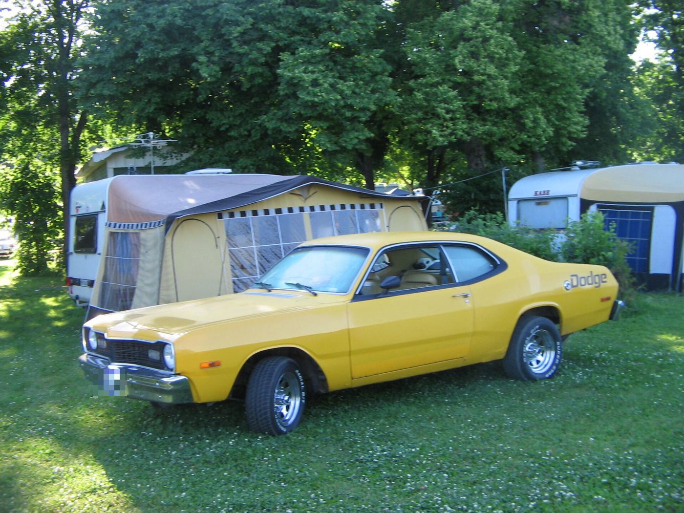 Yellow 1975 Dodge Dart Sport fastback coupe parked on grass beside a caravan awning