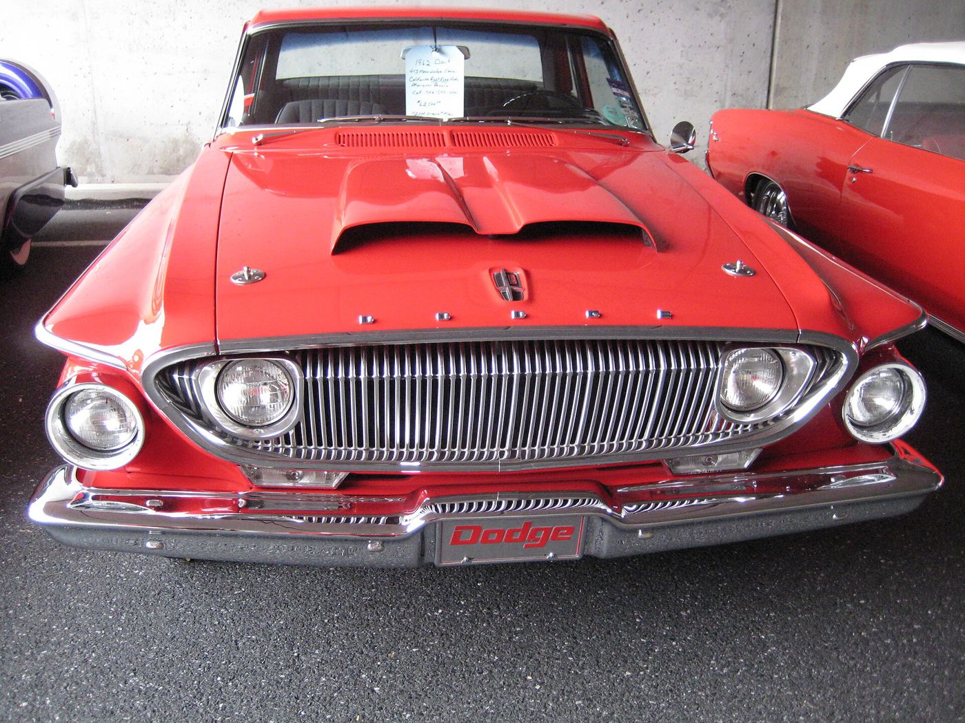 Head-on view of a red 1962 Dodge Dart, showing its oval grille, outboard headlamps and raised hood scoop