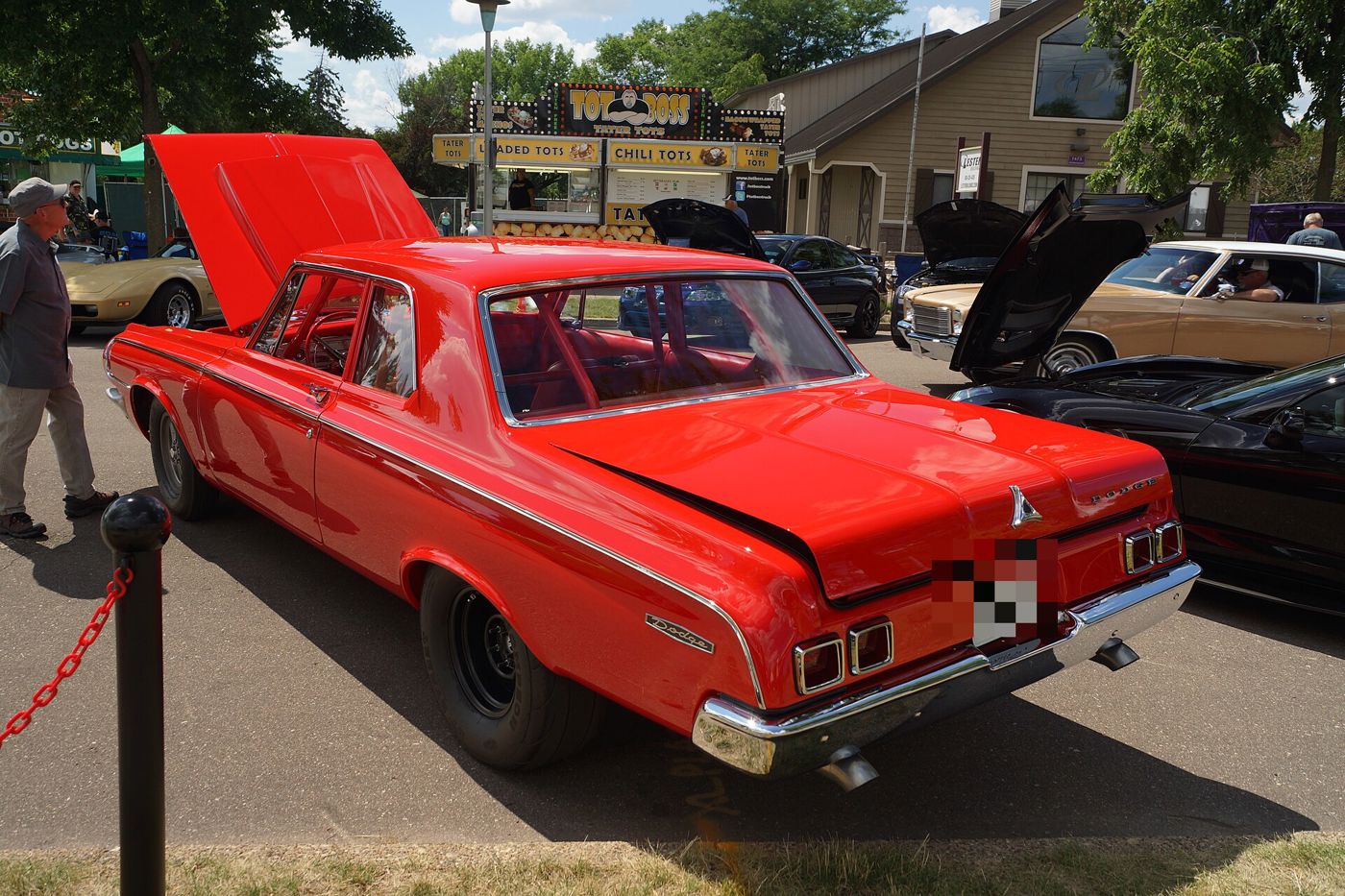 Red 1964 Dodge 330 two-door sedan with the hood up at an outdoor show, seen from the rear three-quarter