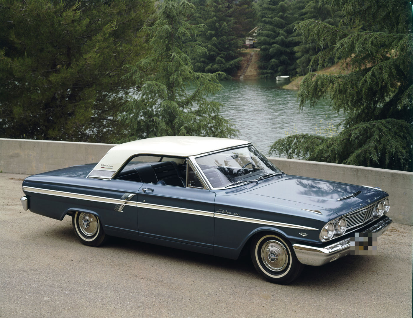 Blue 1964 Ford Fairlane 500 Sports Coupe with a white roof, front three-quarter view beside a lake, 289 emblem on the front fender