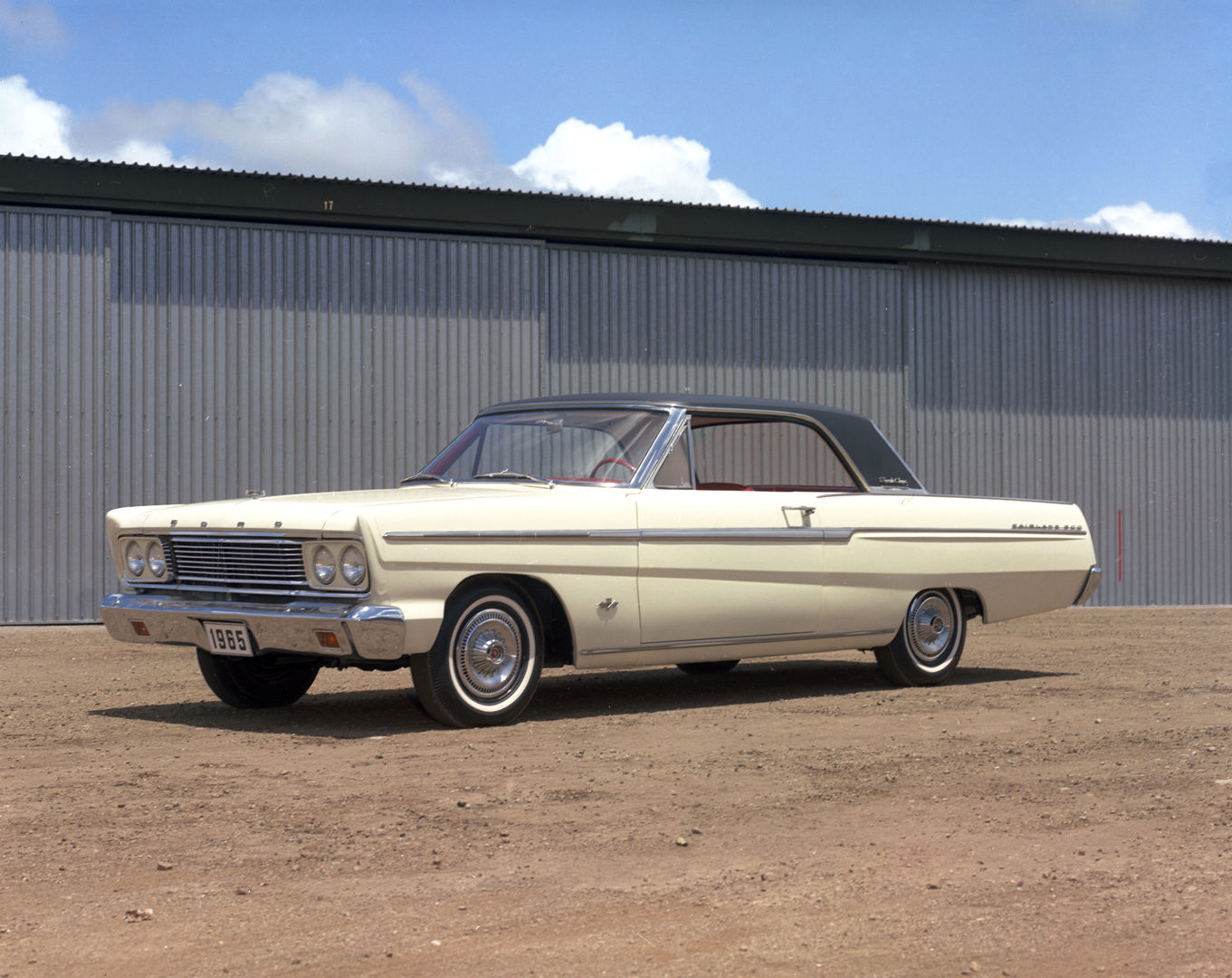 Cream 1965 Ford Fairlane 500 Sports Coupe with a black roof, front three-quarter view in front of a corrugated metal building