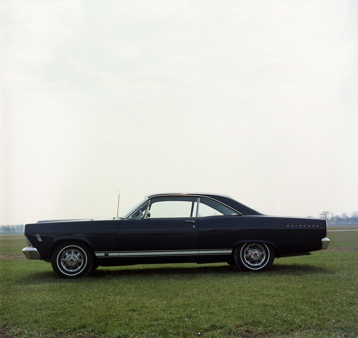 Dark blue 1966 Ford Fairlane two-door hardtop in profile on a grass field, with a white rocker stripe and styled wheel covers