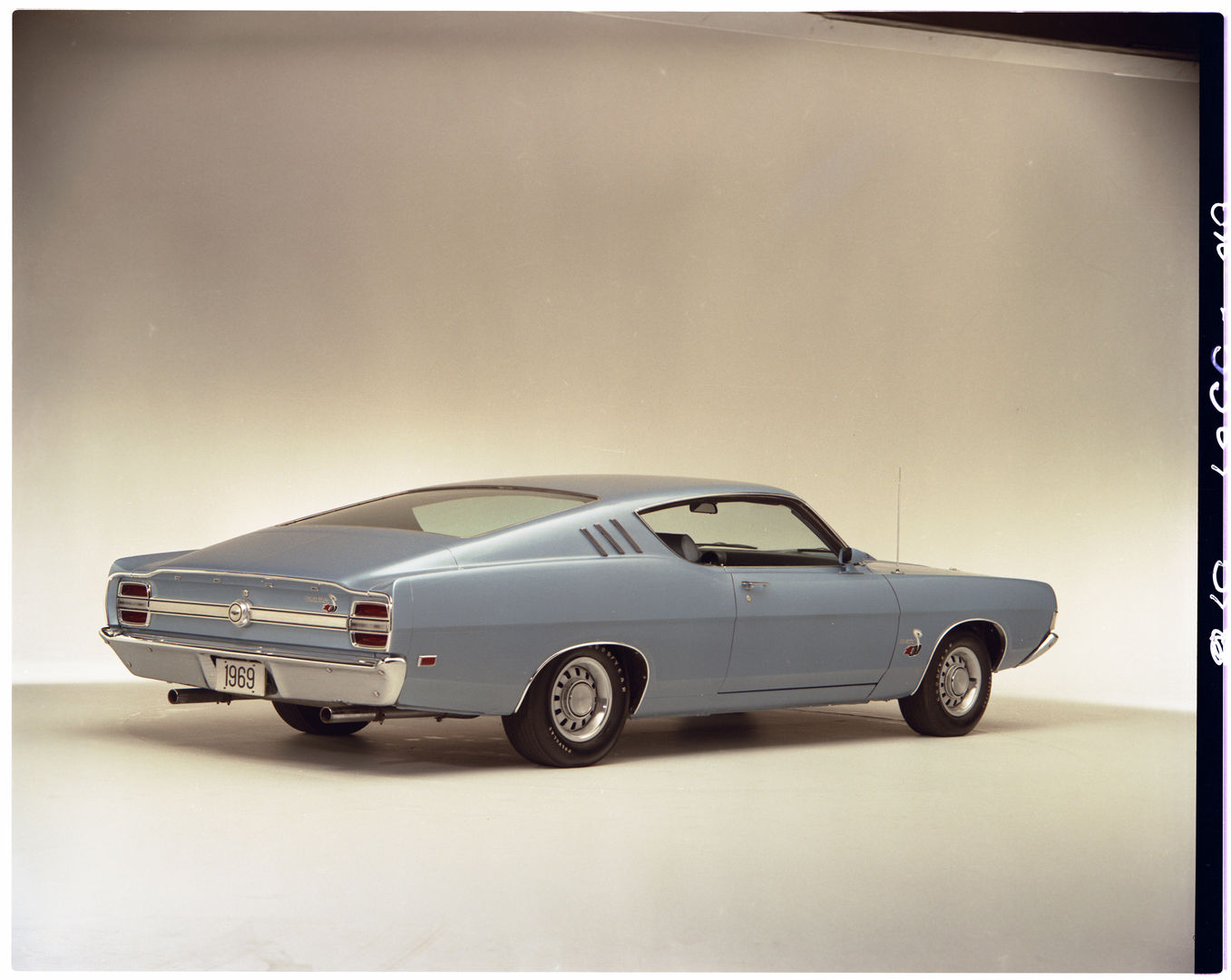 Light blue 1969 Ford Fairlane Cobra SportsRoof in a studio, rear three-quarter view, with Cobra emblems on the rear panel and front fender and dual exhaust tips