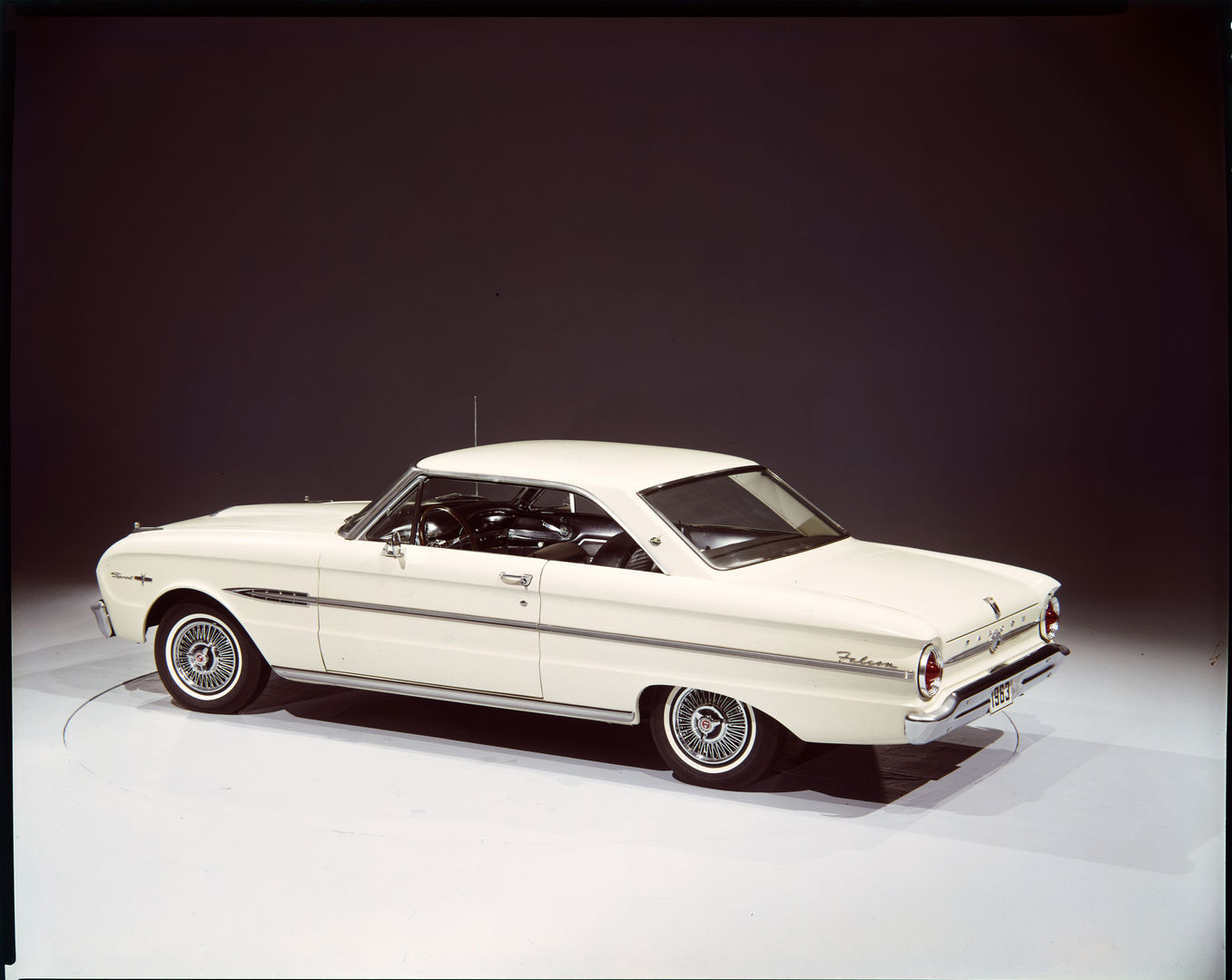 White 1963 Ford Falcon Sprint two-door hardtop in a studio, seen from a high rear three-quarter, with wire wheel covers and Sprint script on the front fender