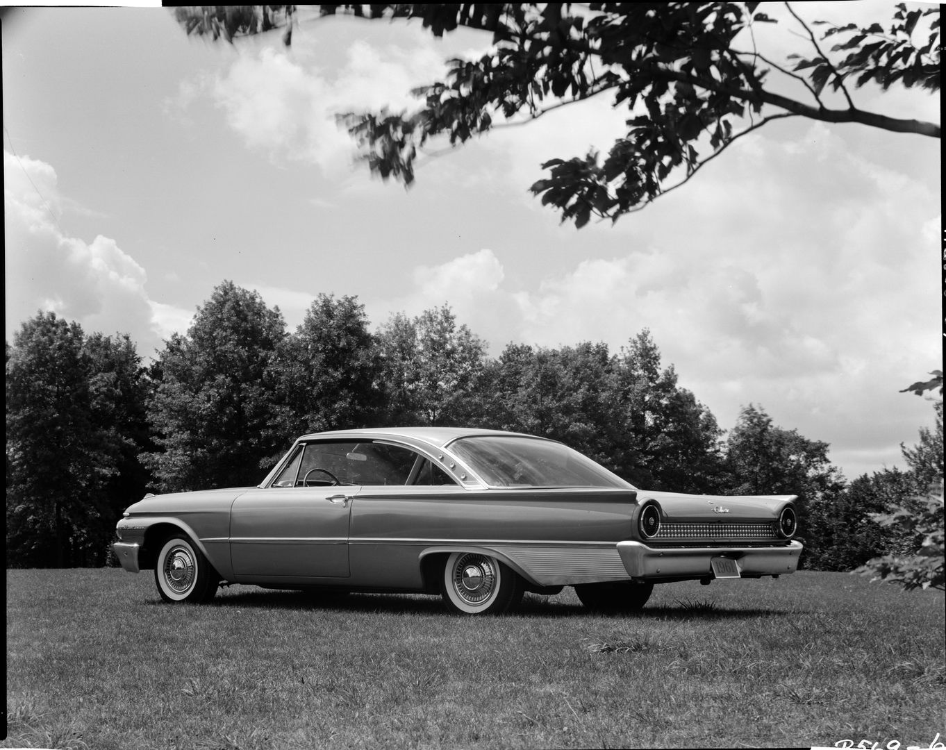 Black-and-white photo of a 1961 Ford Galaxie Starliner two-door hardtop on a lawn, rear three-quarter view, showing the thin-pillar fastback roof and round taillights