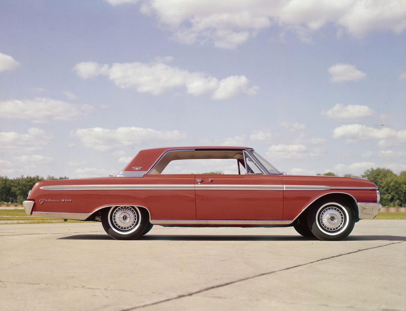 Red 1962 Ford Galaxie 500 two-door hardtop in full side profile on concrete under a partly cloudy sky
