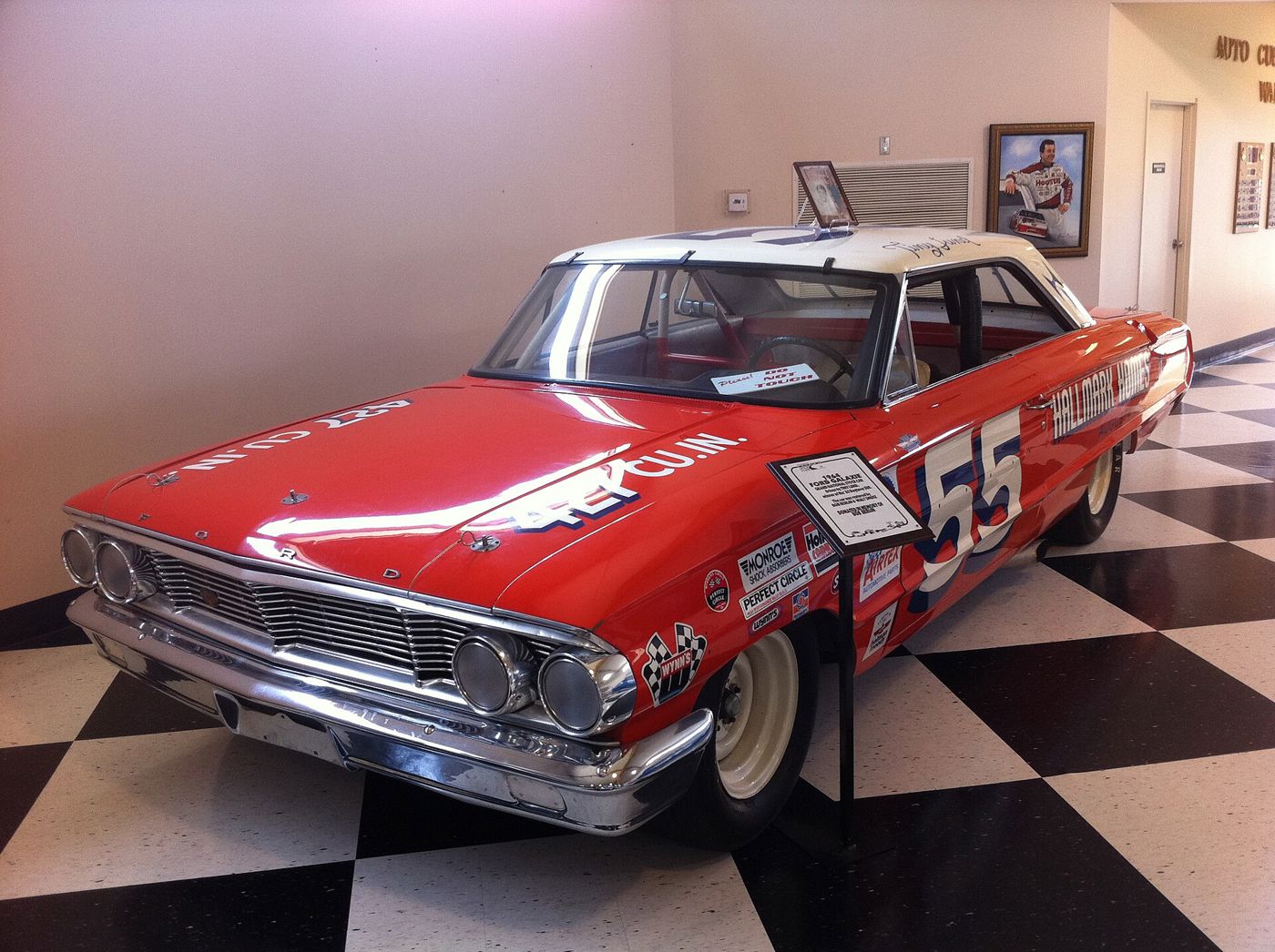 Red and white 1964 Ford Galaxie NASCAR race car, number 55, with 427 cubic inch hood lettering and sponsor decals, displayed on a checkered museum floor