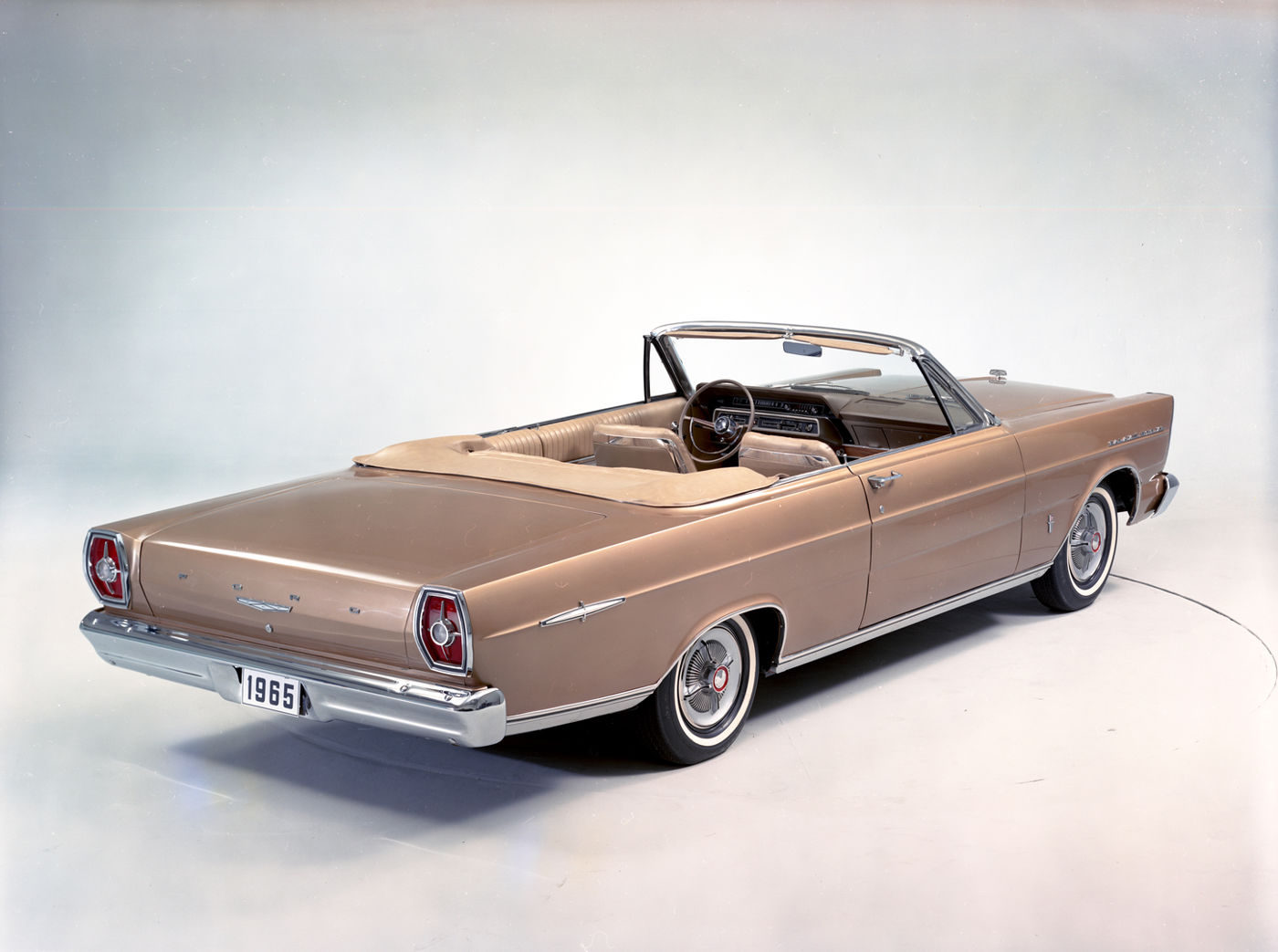 Bronze 1965 Ford Galaxie 500XL convertible with a tan interior and the top down, high rear three-quarter studio view