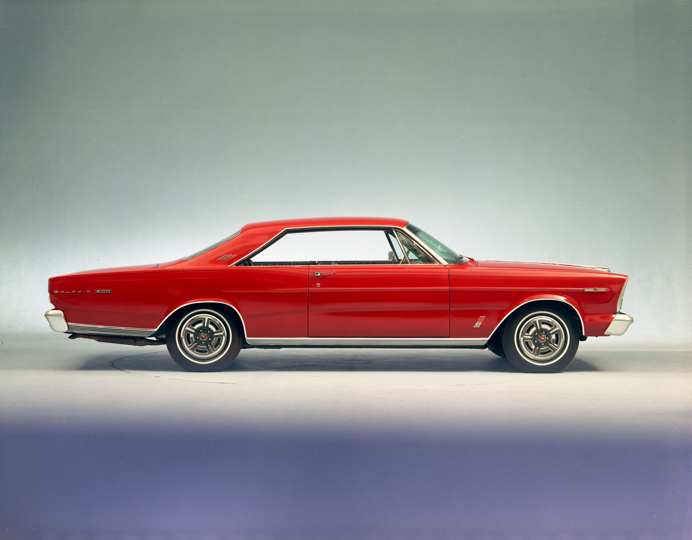 Red 1966 Ford Galaxie 500 7-Litre fastback hardtop in full side profile in a studio, with styled steel wheels and Galaxie 500 lettering on the rear fender