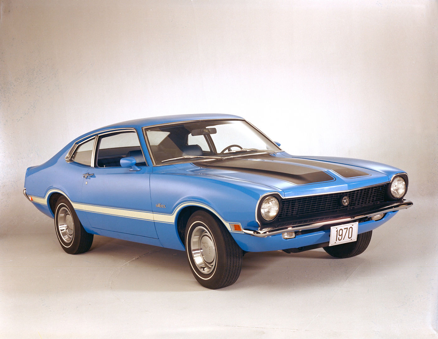 Bright blue 1970 Ford Maverick Grabber two-door with a black hood, a white body-side stripe and a black grille, front three-quarter studio view