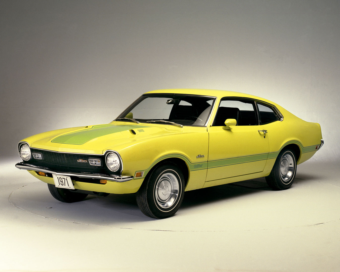 Yellow 1971 Ford Maverick Grabber two-door with green hood and side stripes, front three-quarter studio view