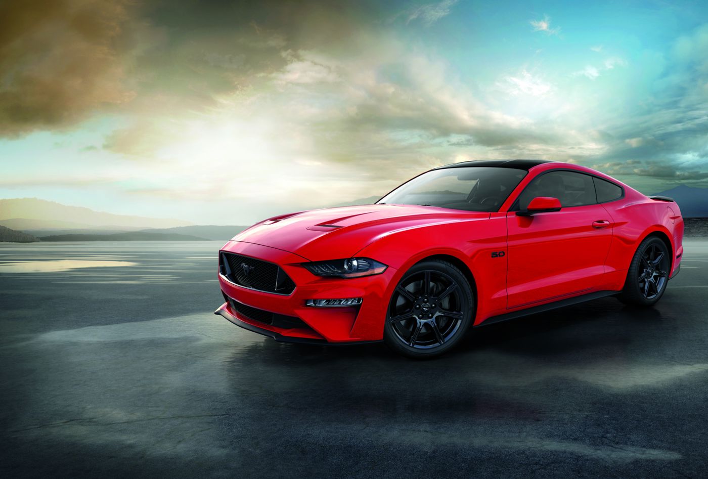Red 2018 Ford Mustang GT fastback with a black roof and black wheels on a wet lakeside apron under a dramatic sky, front three-quarter view