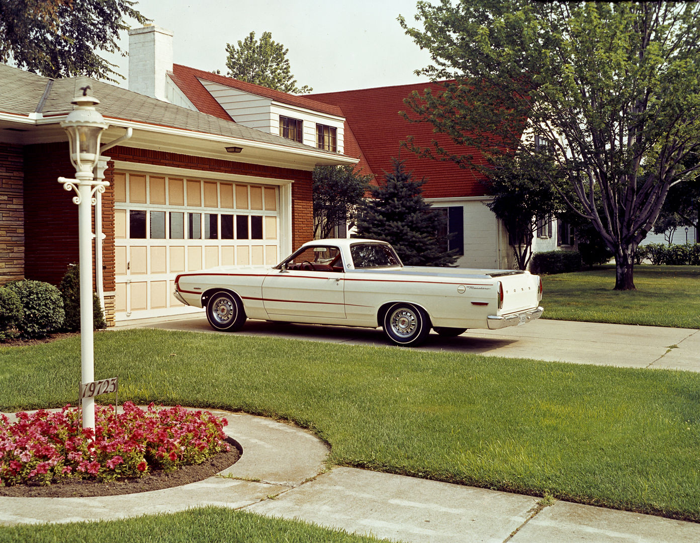 White 1968 Ford Ranchero GT with a red body-side stripe parked in a suburban driveway beside a garage and a flower bed