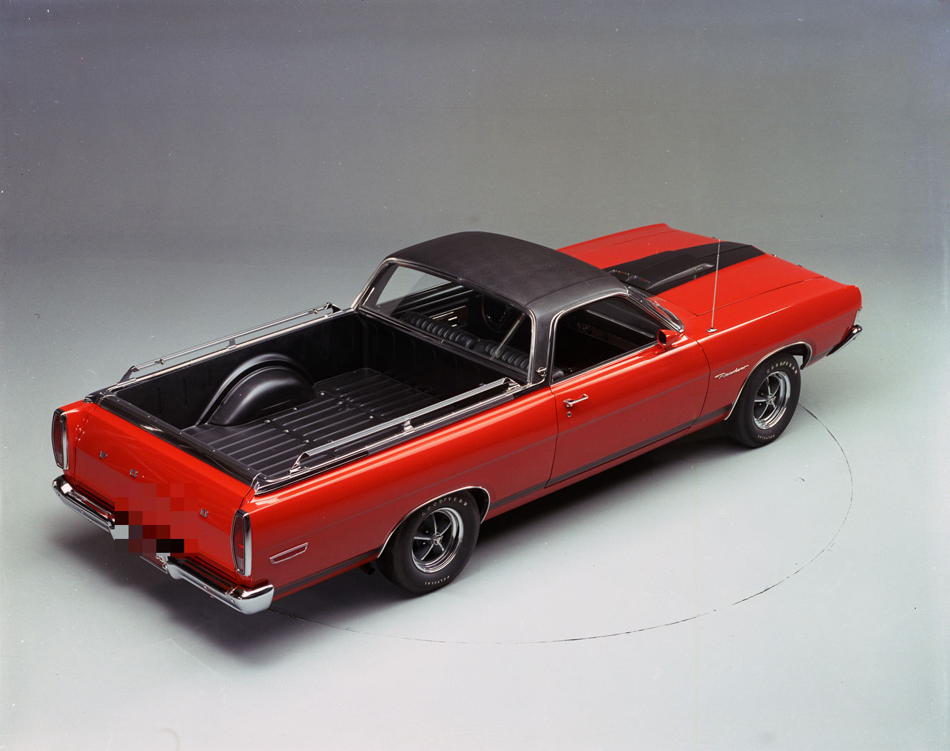 High rear three-quarter studio view of a red 1969 Ford Ranchero GT with a black roof, showing the black-lined cargo bed and bed rails