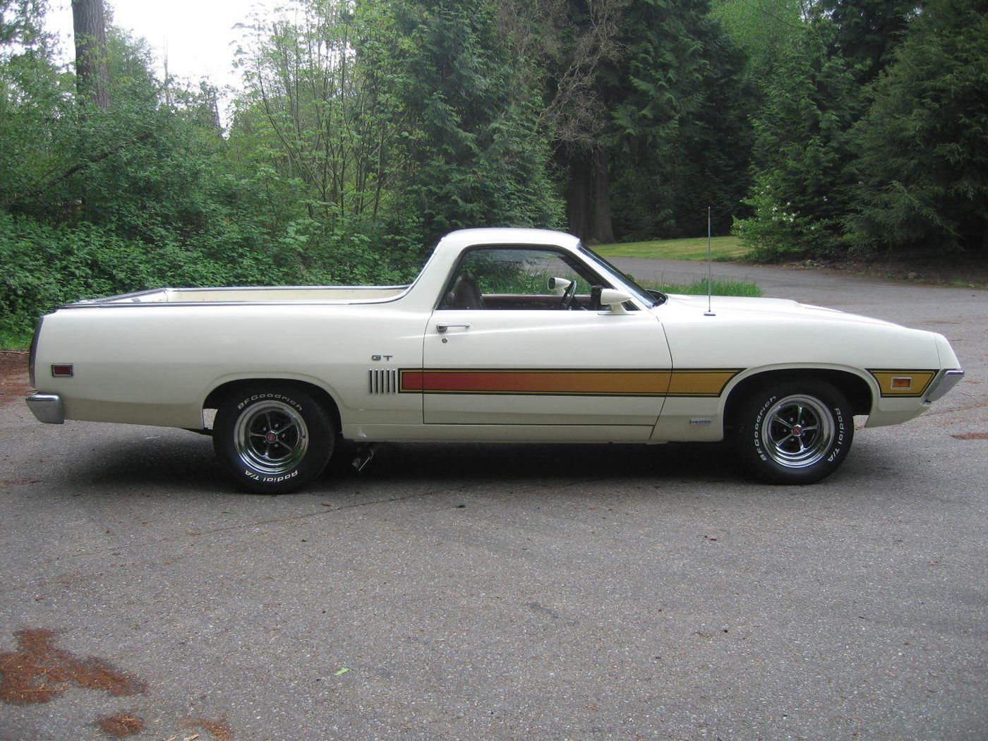 White 1970 Ford Ranchero GT in side profile on a paved lot, with a gold and red laser side stripe, GT door lettering and Magnum 500 wheels
