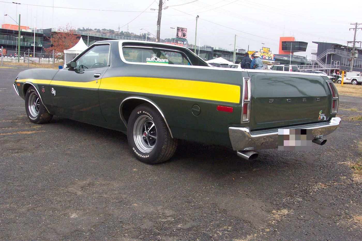 Dark green 1972 Ford Ranchero GT with a yellow side stripe and Magnum 500 wheels, rear three-quarter view in a car park