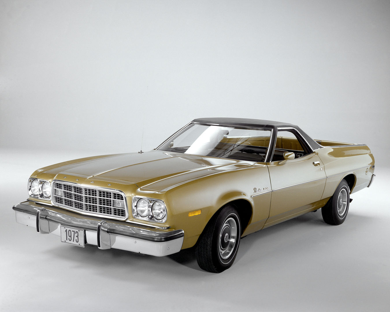 Gold 1973 Ford Ranchero 500 with a black vinyl roof in a studio, front three-quarter view, showing the 1973 grille and energy-absorbing front bumper