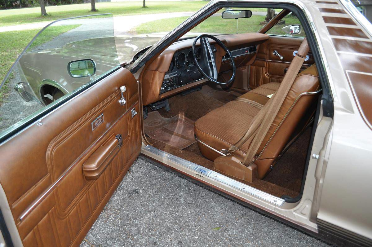 Open driver's door of a 1977 Ford Ranchero GT showing a tan bench seat, door panel, and dashboard
