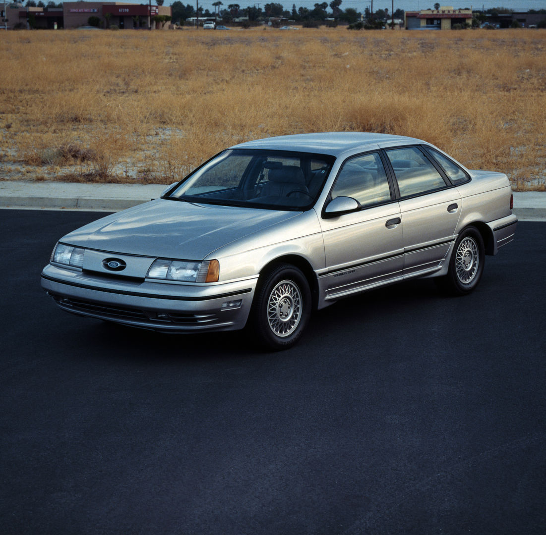 Silver 1989 Ford Taurus SHO sedan, front three-quarter view on desert tarmac, with body-color lower cladding and multi-spoke alloy wheels