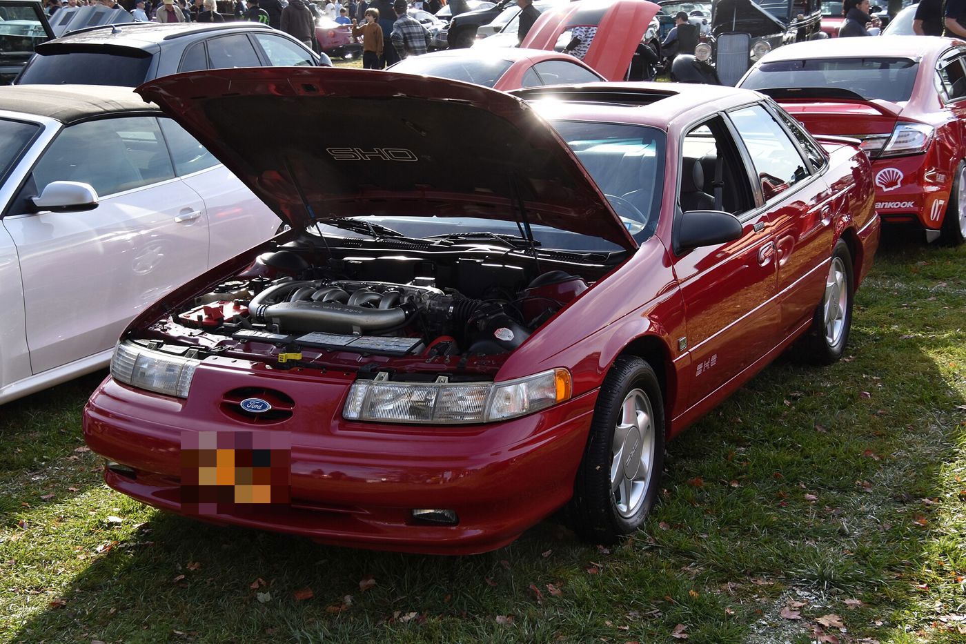 Red 1994 Ford Taurus SHO at an outdoor car show with the hood raised, showing the Yamaha-built SHO engine and the SHO emblem under the hood