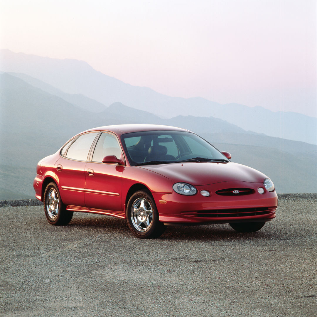 Red 1996 Ford Taurus SHO with the oval third-generation styling, front three-quarter view on gravel with misty mountains behind