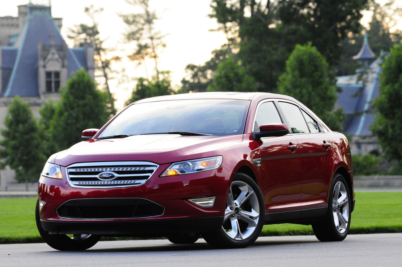 Red 2010 Ford Taurus SHO sedan with a chrome three-bar grille, front three-quarter view before a chateau-style building