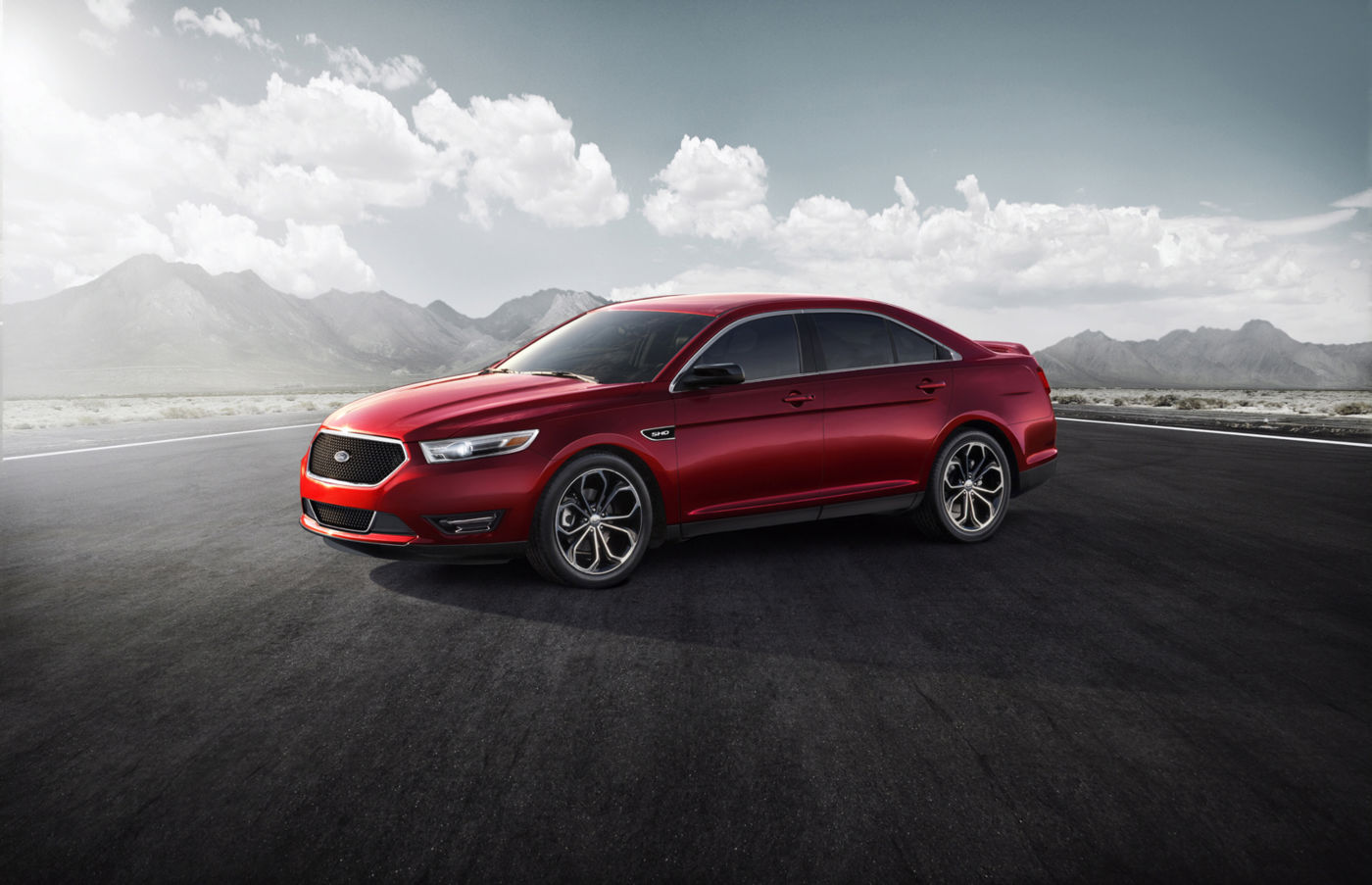 Red 2013 Ford Taurus SHO with the redesigned trapezoidal black mesh grille, front three-quarter view on a wide tarmac with mountains