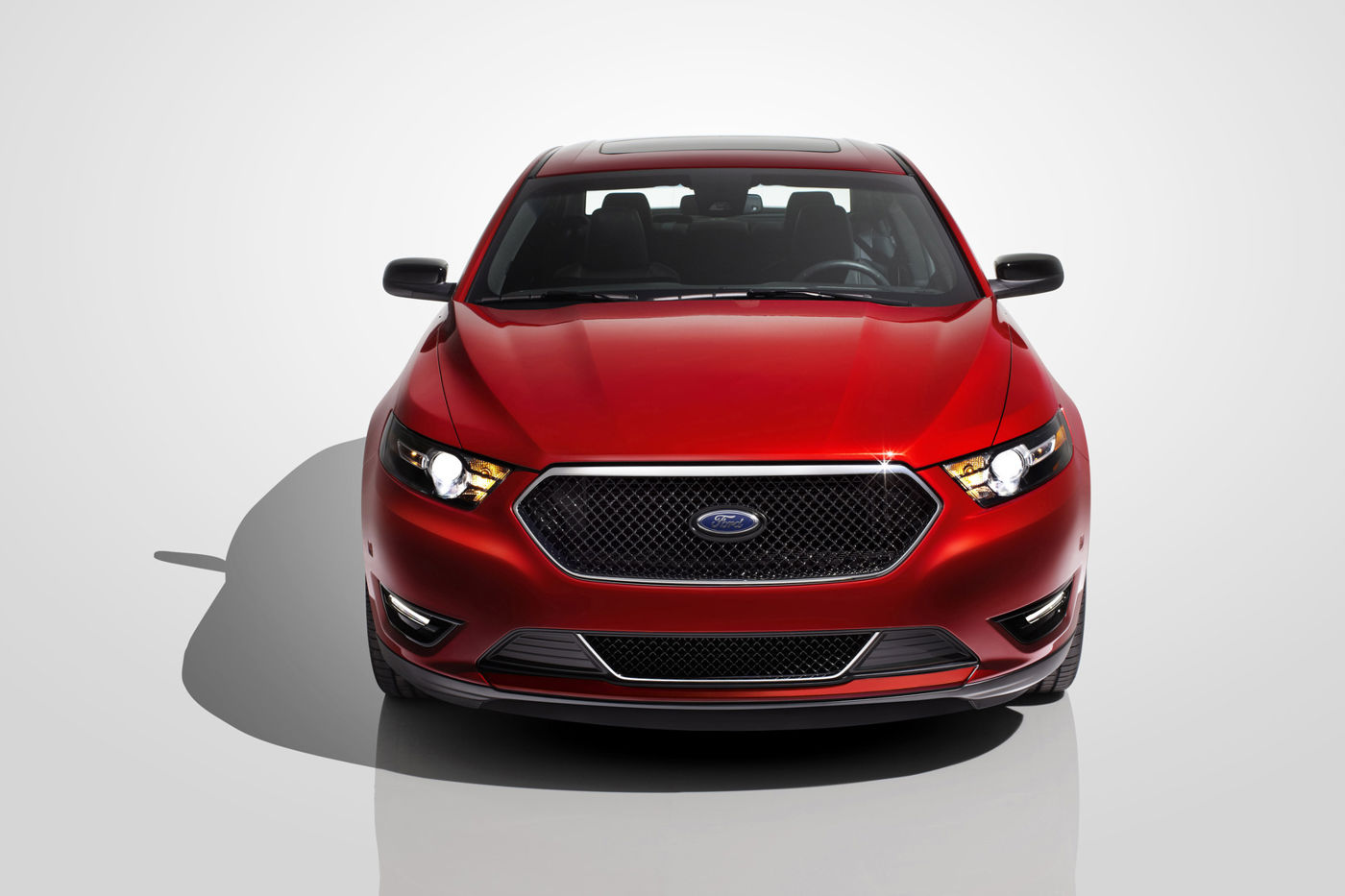 Red 2015 Ford Taurus SHO seen head-on in a white studio, showing the black mesh grille and LED headlamp accents