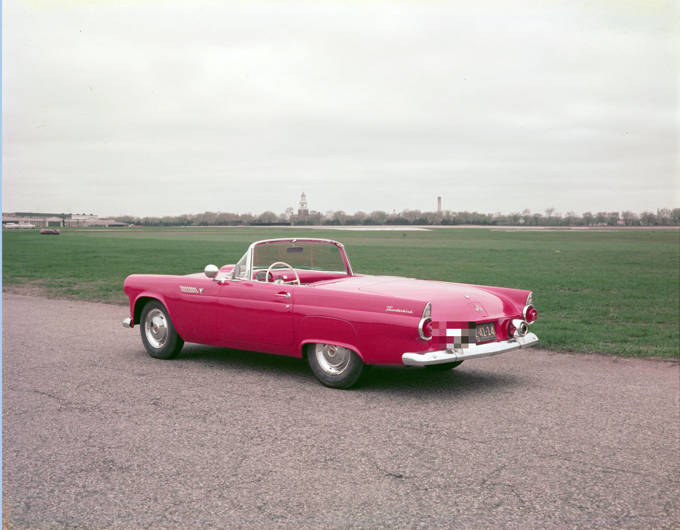 Red 1955 Ford Thunderbird two-seat convertible with the top down, rear three-quarter view on an airfield apron, showing the small round taillights