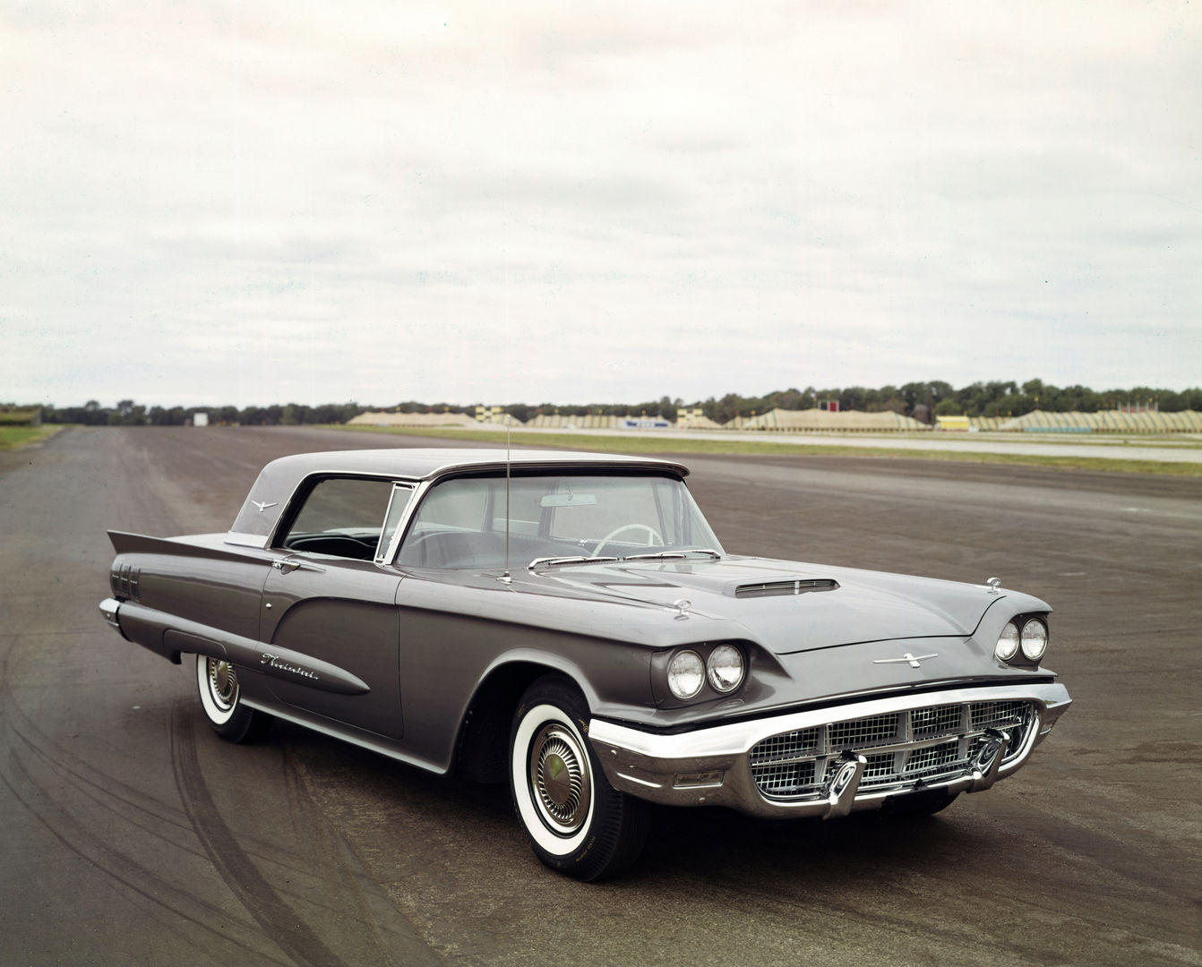 Grey 1960 Ford Thunderbird hardtop on a test-track apron, front three-quarter view showing the triple-taillight era front with a hood scoop