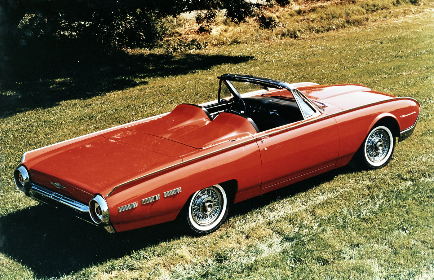 Red 1962 Ford Thunderbird Sports Roadster on grass, high rear three-quarter view, showing the two-headrest fiberglass tonneau over the rear seat and Kelsey-Hayes wire wheels