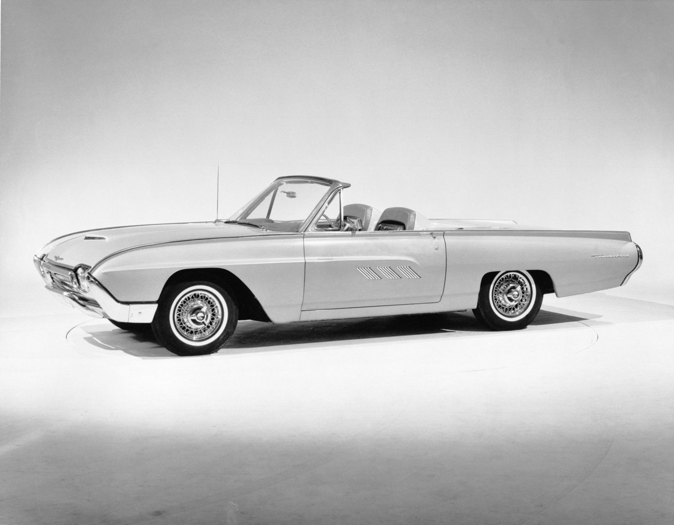 Black-and-white studio photo of a 1963 Ford Thunderbird convertible with the top down, side view, with wire wheels and the 1963 door-line spears