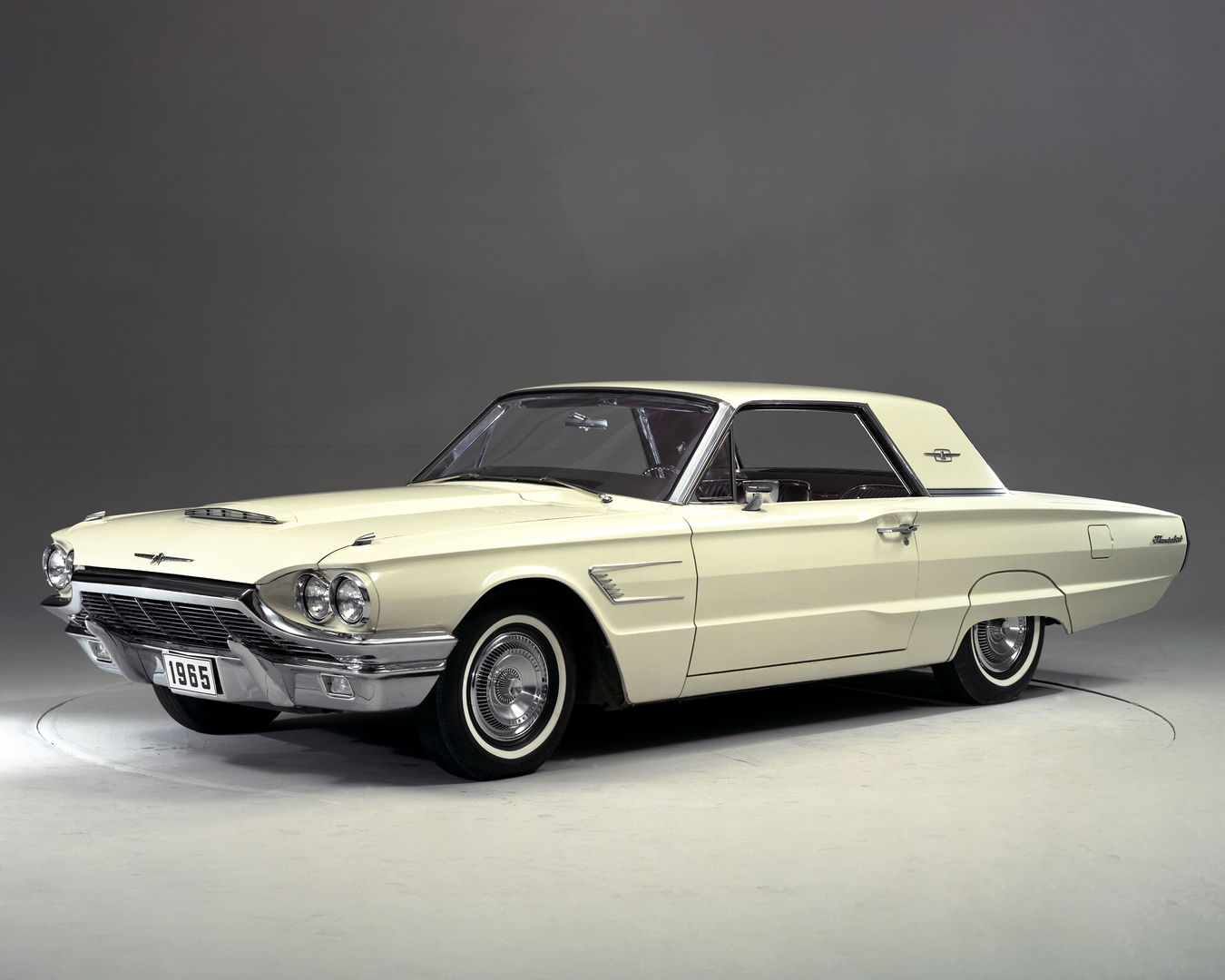 Cream 1965 Ford Thunderbird hardtop on a studio turntable, front three-quarter view