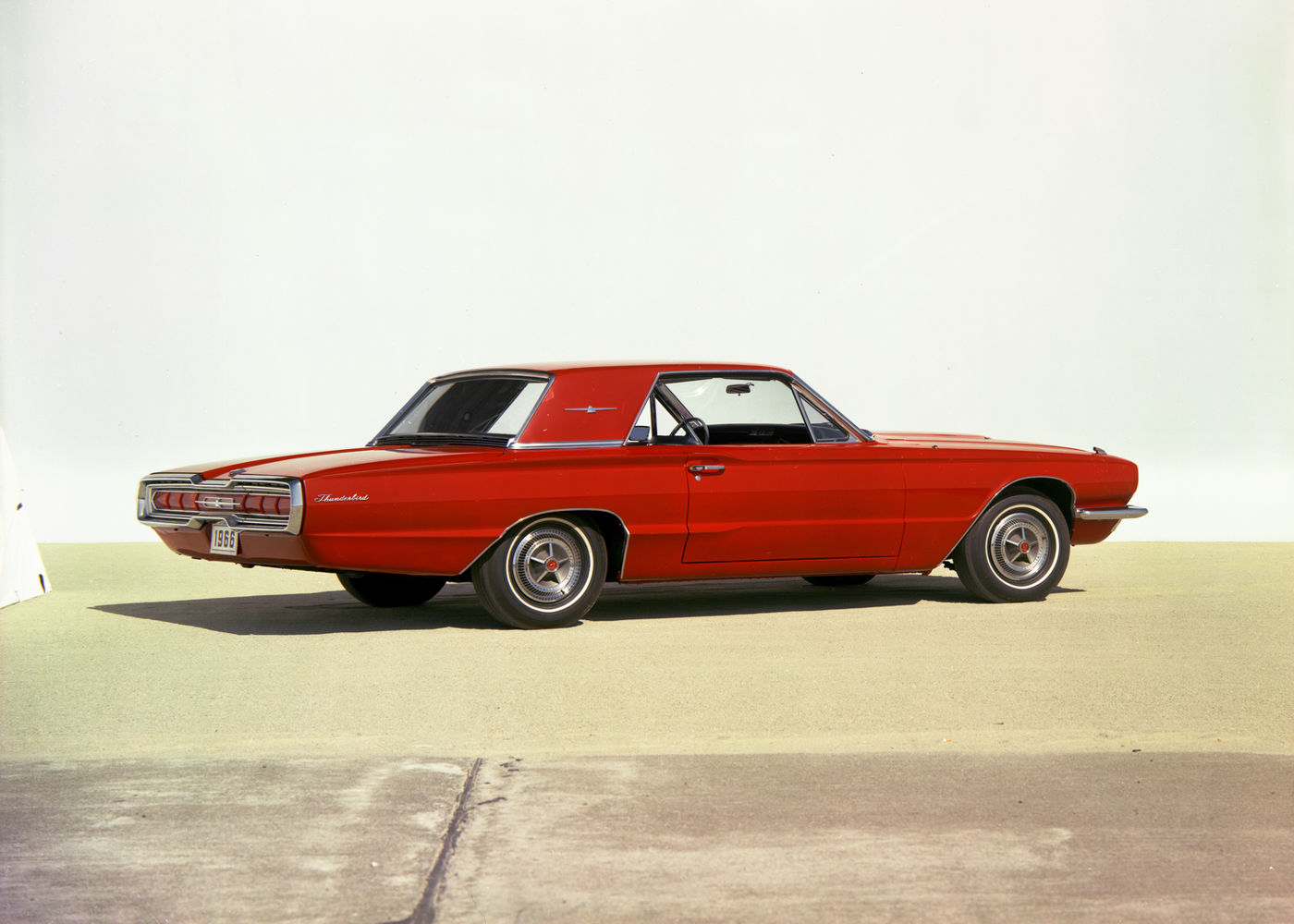Red 1966 Ford Thunderbird hardtop on a pale apron, rear three-quarter view showing the full-width taillight panel