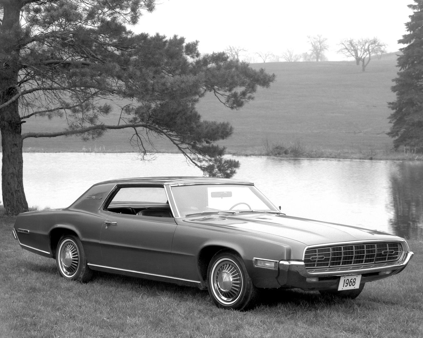 Black-and-white photo of a 1968 Ford Thunderbird two-door hardtop on grass by a pond, front three-quarter view