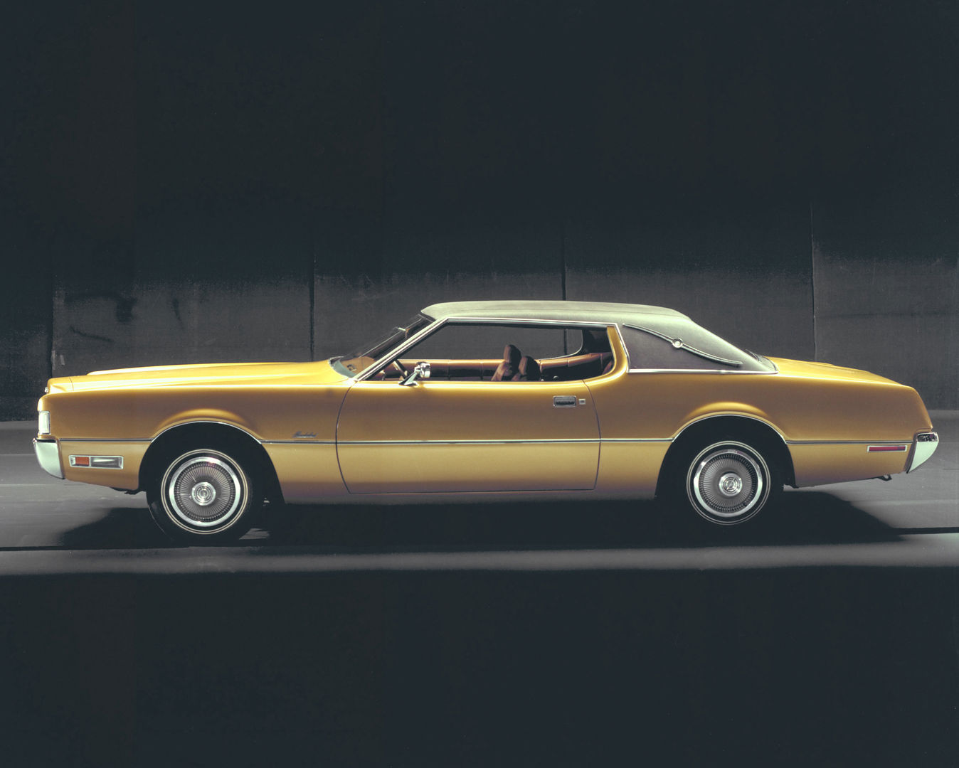 Gold 1972 Ford Thunderbird Landau hardtop with a white vinyl roof, side profile on a dark studio set